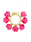 A gold-tone bracelet with hot pink iridescent petal charms attached to it, secured with a toggle closure.
