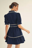 Woman wearing a navy dress with white trim on a beige background