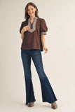 Woman wearing a brown blouse with stripe details and blue flared jeans on a beige background