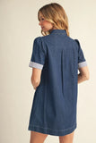 Woman wearing a blue denim dress with white trim on a beige background
