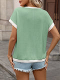 Woman wearing a green and white top with denim shorts on a city street.