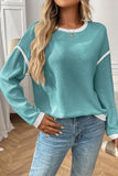 Person wearing a teal sweater with white trim and blue jeans indoors.