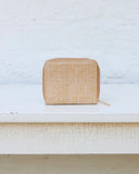 Beige woven wallet on a white surface with a light blue textured background