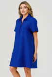 A woman modeling a short-sleeve collared shift dress in a vibrant royal blue color, photographed against a neutral light gray studio background.