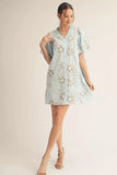 Woman wearing a light blue dress with floral embroidery on a plain background