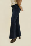 A model wearing dark blue flare jeans and brown block-heel boots, shown from the waist down against a solid beige background.