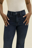 A close-up of a model wearing dark blue denim jeans with a cream ribbed top, showing the fit from the waist down against a solid light beige background.