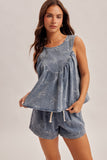 Woman wearing a denim romper with white embroidery on a plain background