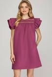 Woman wearing a purple dress with ruffled sleeves on a gray background