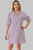 A woman modeling a short puff-sleeve shirt dress with vertical purple and white stripes, featuring a button-down front and collar, set against a solid gray background.