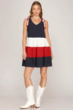 Woman wearing a red, white, and blue dress with white cowboy boots on a plain background