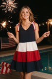 Woman in a red, white, and blue dress holding sparklers by a pool with fireworks in the background.