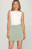 Woman wearing a white top and light green skirt on a plain background