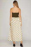 Woman wearing a strapless top and polka dot skirt on a plain background
