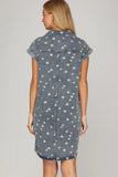 Woman wearing a denim dress with white floral patterns on a plain background