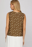Woman wearing a brown sleeveless top with white polka dots on a plain background