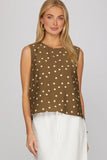 Woman wearing a brown sleeveless top with white polka dots on a plain background