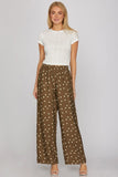 Woman wearing a white top and brown patterned pants on a plain background