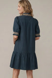 Woman wearing a dark blue dress with decorative trim on a beige background