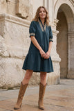Woman in a teal dress with gold trim standing in front of an old stone building.