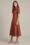 A woman modeling a rust-colored short-sleeve midi dress with a collared neckline and front button placket, paired with beige heeled sandals, against a solid light beige studio background.