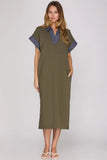 A woman modeling a short-sleeve olive green kaftan dress with a blue and white striped V-neck collar and matching striped sleeve cuffs, paired with white sandals, against a light gray studio background.