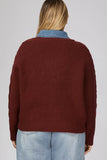 A woman viewed from the back wearing a ribbed knit sweater in deep burgundy over a light blue denim shirt collar, paired with light-wash jeans, against a plain light gray studio background.