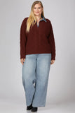 A woman modeling a burgundy cable-knit polo sweater over a light blue collared shirt, paired with light-wash wide-leg jeans and black shoes, against a solid gray studio background.