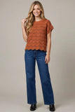 Woman wearing a rust-colored top and blue jeans on a beige background