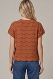 Woman wearing a brown patterned top and blue jeans on a beige background