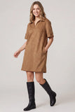 A woman modeling a tan-brown short-sleeve collared shirt dress with side pockets, paired with black knee-high leather boots, against a light gray studio background.
