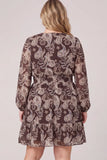 A woman viewed from the back wearing a sheer long-sleeve mini dress with an intricate paisley and floral pattern in brown, beige, and white, set against a plain light beige studio background.