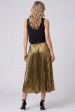 A woman shown from the back wearing a sleeveless black top and a shiny metallic gold pleated midi skirt, paired with black high heels, against a light gray studio background.