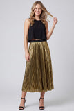 A woman modeling a sleeveless black crop top and a high-waisted, pleated metallic gold midi skirt with black ankle-strap heels, set against a light gray studio background.