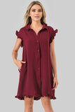 A woman modeling a short-sleeve button-front dress in deep burgundy with ruffled sleeves and hem, photographed against a plain light gray studio background.
