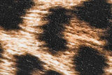 A close-up of a textured animal print fabric or material with irregular black patches over a warm tan and cream background.