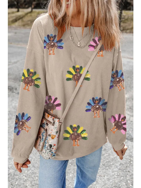 Person wearing a beige sweater with colorful turkey designs, holding a patterned bag.