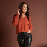 Woman wearing a rust-colored sweater and black pants against a brown background