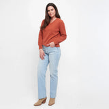 Woman wearing an orange sweater and light blue jeans on a white background