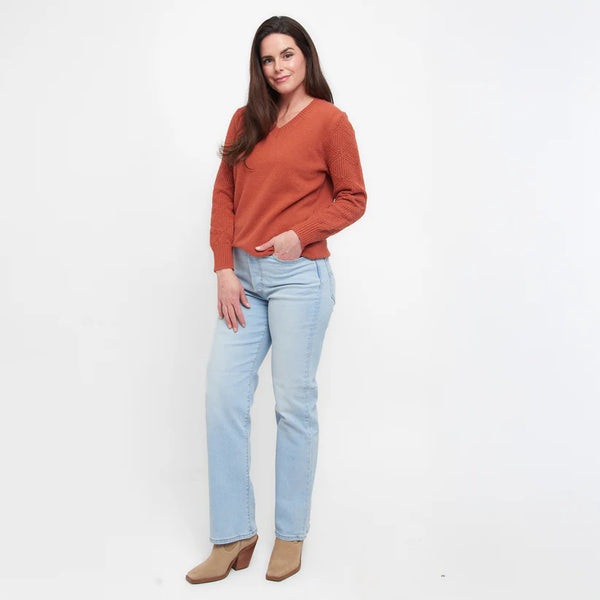 Woman wearing an orange sweater and light blue jeans on a white background