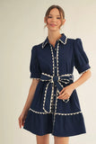 Woman wearing a navy dress with white trim on a beige background