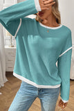 Person wearing a teal long-sleeve top with white trim in a room.
