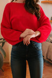 Person wearing a red sweater and blue jeans indoors.