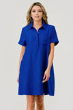 A woman modeling a short-sleeve collared shift dress in a vibrant royal blue color with a subtle textured pattern, set against a plain light gray studio background.