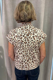 A woman viewed from behind wearing a leopard-print short-sleeve blouse and dark blue jeans, standing in front of a light gray curtain.