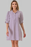 A woman modeling a short-sleeve button-front shirt dress with vertical purple and white stripes, puff sleeves, and a pointed collar against a plain light gray studio background.