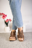 Person wearing brown sandals with a white wall and pink flowers in the background