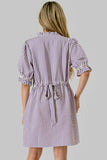 A woman shown from the back wearing a short-sleeve striped shirt dress with a ruffled collar and a drawstring waist, set against a solid gray background.