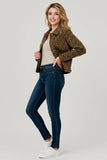 A woman modeling a cropped leopard-print jacket over a beige top and dark blue skinny jeans, paired with white sneakers, against a light gray studio background.
