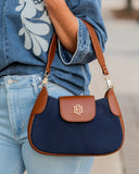 A navy blue and brown shoulder bag with a gold interlocking H logo on the front flap, worn crossbody by a person in a denim shirt and jeans.